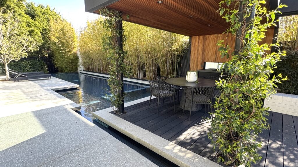 Contemporary outdoor living area with pool, covered dining space, and lush landscaping